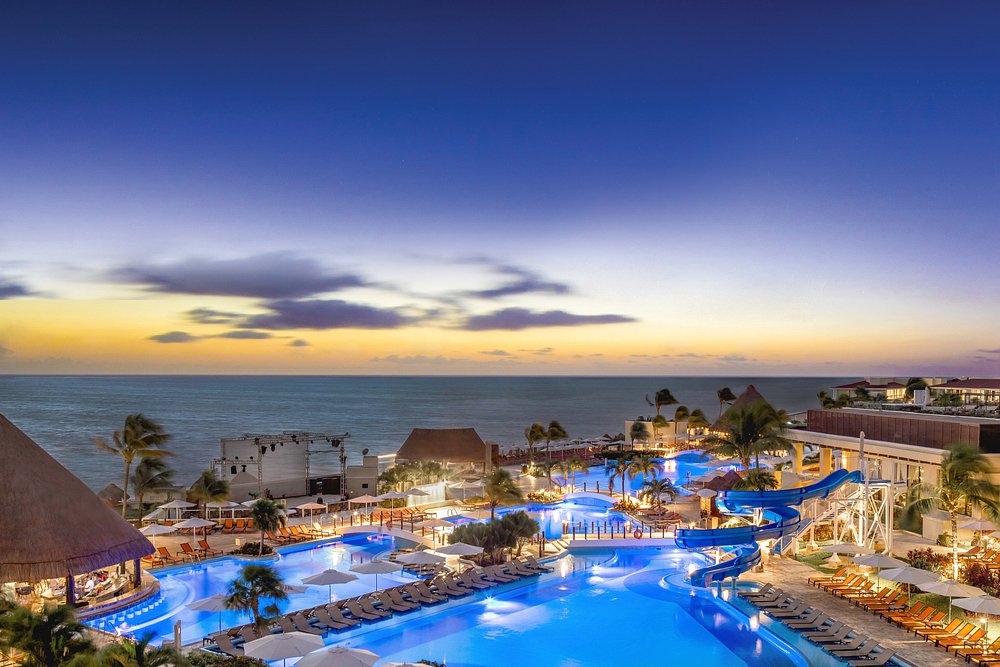 Vista nocturna del resort Moon Palace Cancún con piscinas iluminadas, toboganes de agua y áreas de relajación frente al mar.
