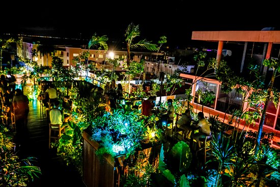 Rooftop terrace at Clandestino by Soma in the Mexican Caribbean, featuring tropical jungle vibes, vibrant night lighting, and an exclusive lounge atmosphere.