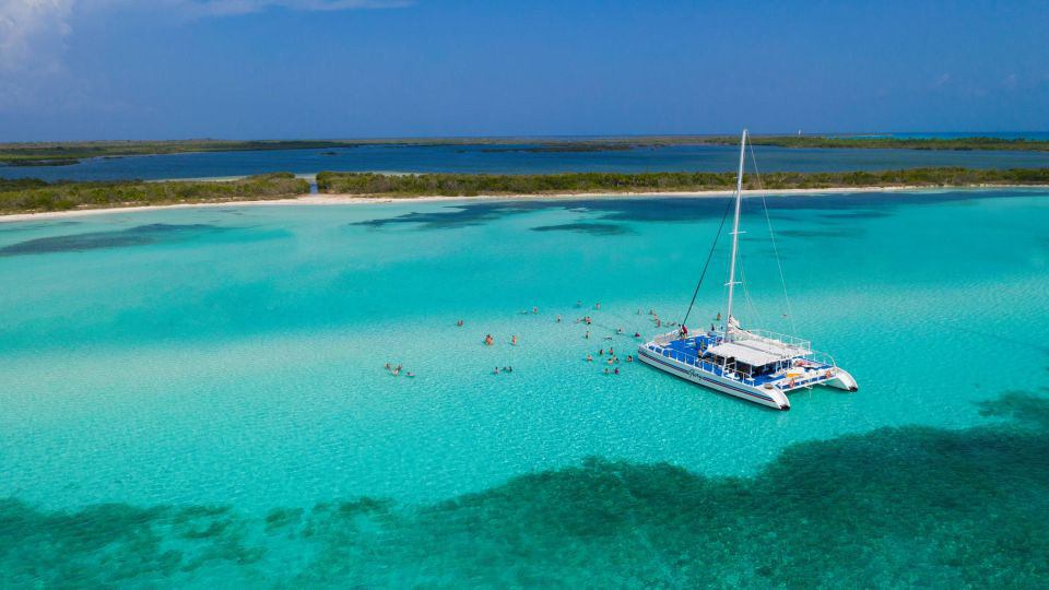Luxury catamaran boat anchored in the crystal-clear turquoise waters of El Cielo, Cozumel, with people snorkeling and enjoying the shallow sandbar.